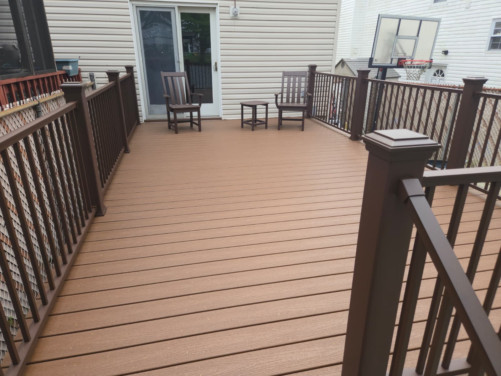 Large composite backyard deck with dark railings and outdoor seating by sliding patio doors.