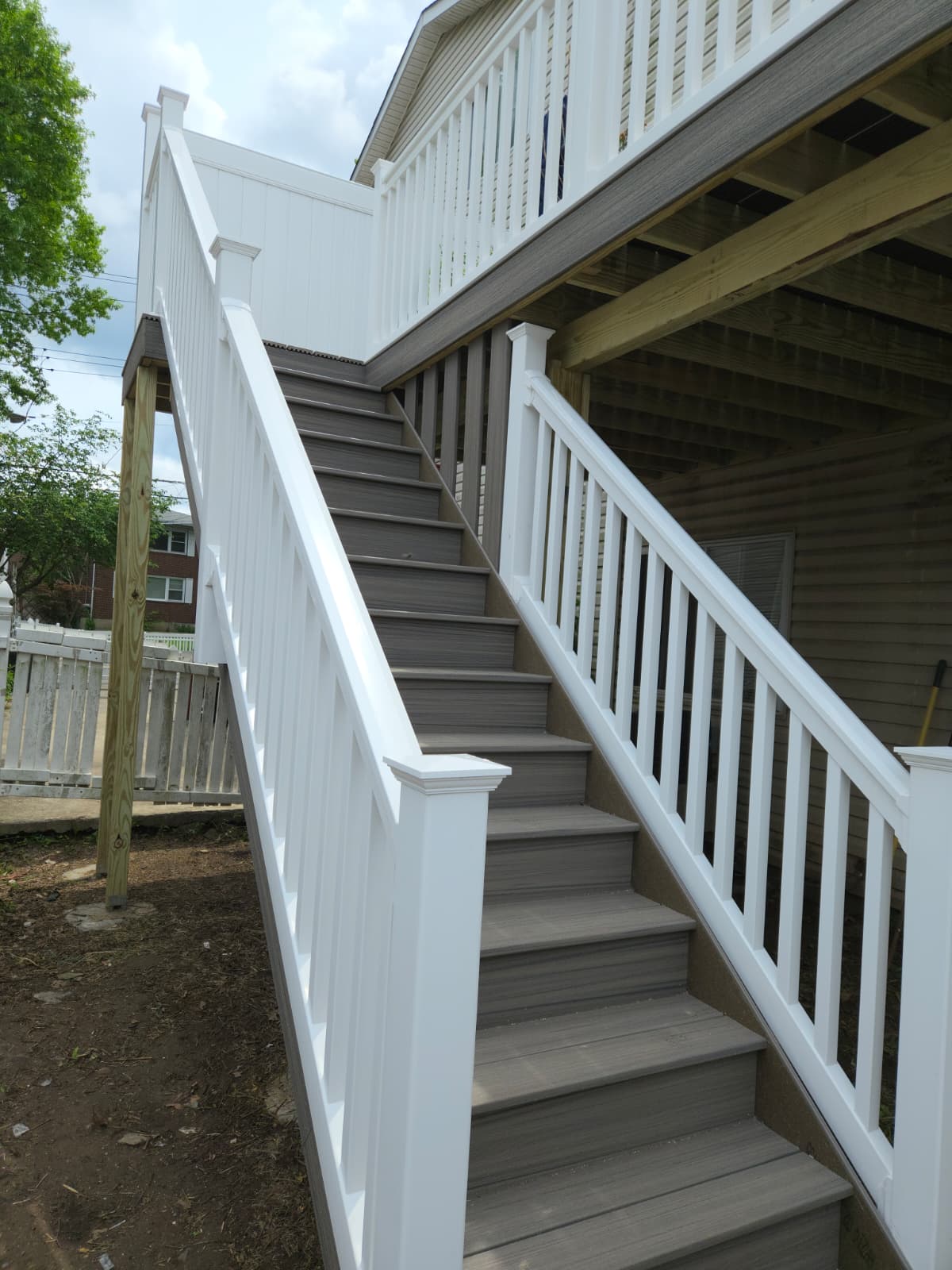 Composite deck stairs with white railings connecting a raised deck to the backyard.